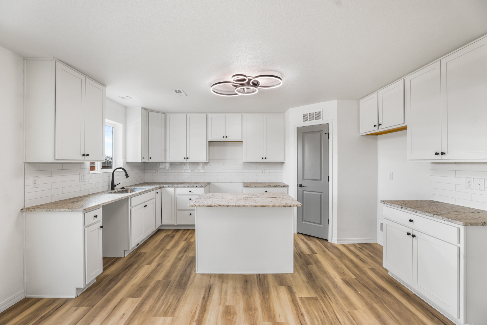 Chieftan kitchen with white shaker cabinets, granite island, and ring chandelier
